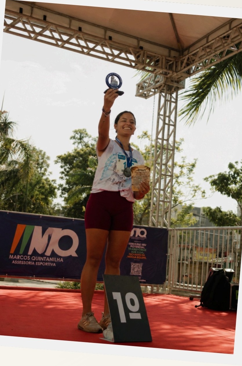 Maria Maria no pódio de uma corrida, segurando o troféu de primeiro lugar